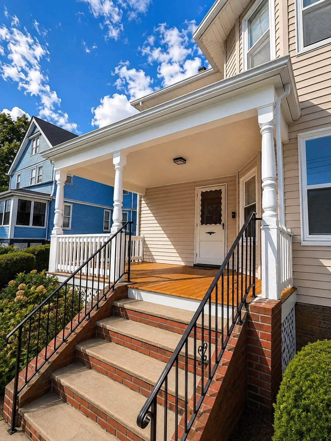 Finished front porch seen from the sidewalk, with a stained wood floor, white rails and brick steps